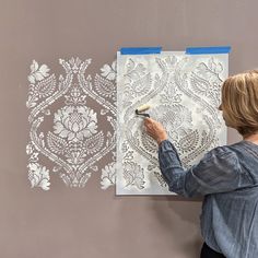 a woman is using a stencil to paint a wall with an intricate design