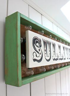 a wooden sign that says sully hanging from the side of a white wall with green trim