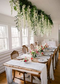 a dining room table with flowers hanging from the ceiling and candles on top of it