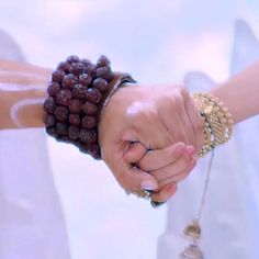 two people holding hands with bracelets on their wrists and one wearing a wedding dress