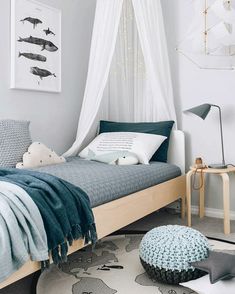 a bed with blue sheets and pillows in a room next to a white curtained window