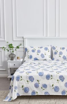 a bed with blue flowers on it in a white room next to a nightstand and table