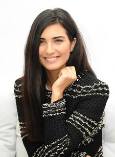 a woman is smiling and posing for the camera with her hand on her chin, wearing a black sweater