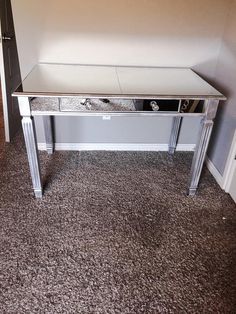 a mirrored desk with silver legs and drawers in a corner room next to a door