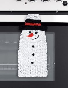 a white knitted snowman sweater hanging from an oven door with buttons on it