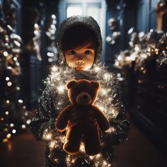 a little boy holding a teddy bear in front of a christmas tree filled with lights