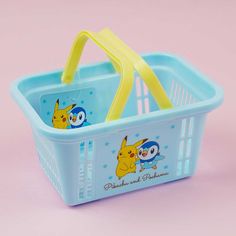 a blue plastic basket with pokemon pictures on the side and yellow handles, sitting on a pink surface