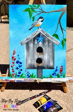 a bird house painted on an easel with paintbrushes