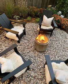 an outdoor fire pit surrounded by chairs and gravel with pillows on them, in the middle of a garden