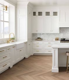 a large kitchen with white cabinets and wood floors is pictured in this image, there are two bar stools at the center of the island