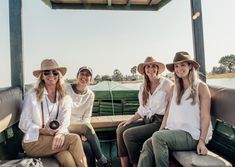 three women sitting on the back of a boat smiling at the camera while wearing hats