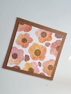 an orange and pink flowered card on a white surface with a brown border around it