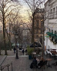 people are sitting at tables in the middle of an alleyway with trees and buildings