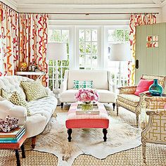 a living room filled with lots of furniture and colorful curtains on the window sill