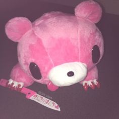 a pink teddy bear laying on top of a floor next to a toothbrush in its mouth