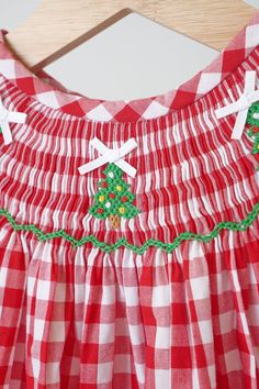 DESCRIPTION Get into the holiday spirit with our Red Christmas Tree Hand Smocked Gingham Romper! This festive and fun romper features a charming red gingham print and a playful smocked Christmas tree design. Perfect for family gatherings and photo ops. Cotton is generally considered a good choice for baby skin for several reasons: Softness: Cotton fabric is naturally soft and gentle against the skin. Breathability: Cotton is highly breathable and allows air to circulate, helping to regulate a baby's body temperature. This breathability makes it suitable for both warm and cool weather. Hypoallergenic: Pure cotton is generally hypoallergenic and less likely to cause allergic reactions. Absorbency: Cotton has excellent moisture-absorbing properties. It can quickly wick away moisture from the Fall Red Smocked Top With Smocked Back, Smocked Christmas Tree, Smocked Christmas Ornaments, Smocked Christmas Dress, Smocked Christmas Dresses Baby, Nice Rompers, Sequin Crafts, Smocked Clothes, Plaid And Leopard