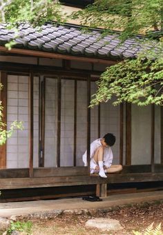 a man sitting on a wooden bench in front of a building next to some trees