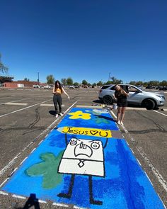 two girls are standing in the parking lot with chalk drawings on the ground and one girl is holding her hand out