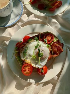 two white plates with food on them sitting on a table next to cups and saucers