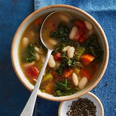 a bowl of soup with beans, kale and carrots next to a spoon