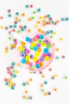 a pink bowl filled with lots of different colored sprinkles next to a spoon