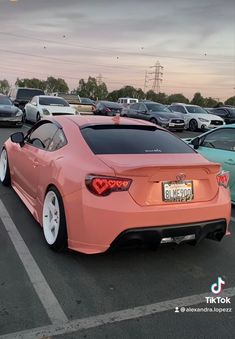 the back end of a pink sports car in a parking lot with many other cars