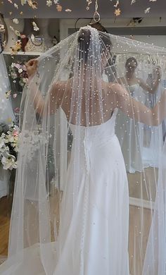 a woman in a white wedding dress is holding her veil over her head and looking at herself in the mirror