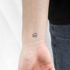 a woman's wrist with a small house tattoo on the left side of her arm