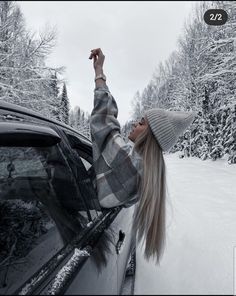 a woman leaning out the window of a car in snow covered forest with her hand up