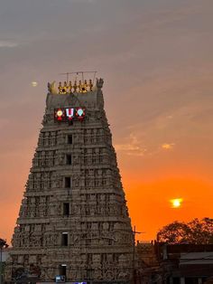 the sun is setting behind a tall tower with statues on it's sides in front of an orange sky