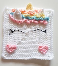 a crocheted square with a cat's face and a rainbow colored crown on top