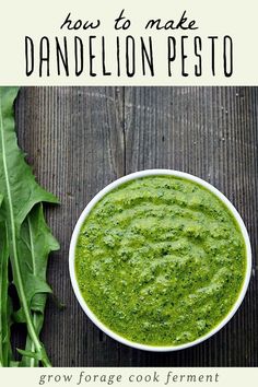 a bowl filled with green pesto next to some leafy greens on a wooden table