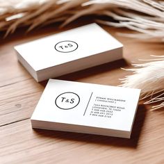 two white business cards sitting on top of a wooden table next to some dried feathers