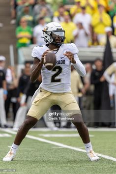 a football player throwing a ball on the field with people watching in the stands behind him