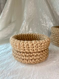 two crocheted baskets sitting on top of a white cloth covered tablecloth,