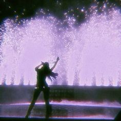 a woman standing in front of a water fountain with her arms up to the sky