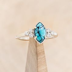 a turquoise stone ring sitting on top of a wooden stand with white diamonds around it