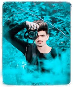 a man holding a camera up to his face while standing in front of some bushes