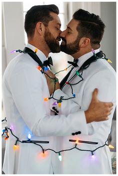 two men dressed in white are kissing each other with christmas lights on their chests