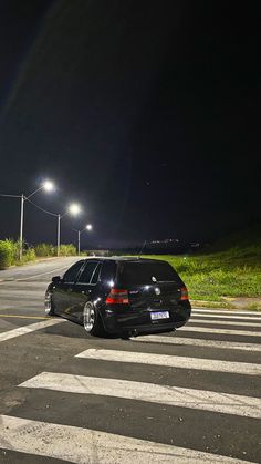 a black car parked in the middle of a crosswalk at night with its lights on