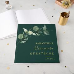 a green guest book sitting on top of a table next to a pen and cup