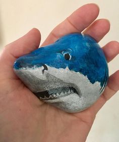 a hand holding a painted rock shaped like a shark