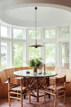 a dining room table with four chairs and a bench in front of large windows that look out onto the woods