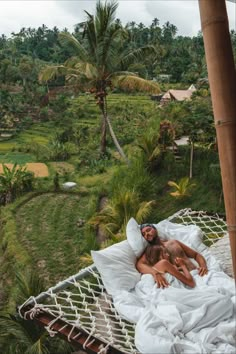 a man and woman laying in a hammock on top of a lush green field