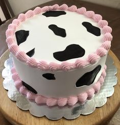 a cake with pink frosting and black spots on it sitting on top of a wooden table