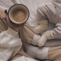 a woman holding a cup of coffee while laying in bed