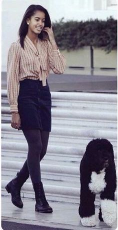 a woman walking next to a black and white dog on the sidewalk with her hand in her hair