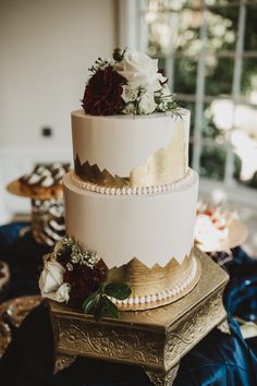 a three tiered wedding cake with white and red flowers on top, sitting on a gold plate