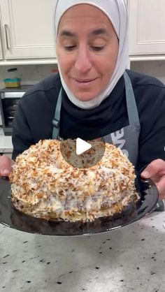 a woman in an apron is holding a cake on a plate with a spatula