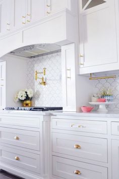 a kitchen with white cabinets and gold hardware on the hood, counter tops and drawers